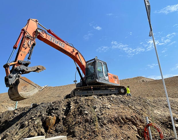 An orange excavator is working on a pile of dirt for an excavation contractor.