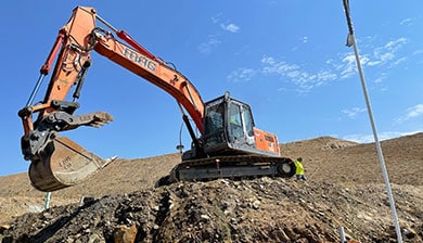 An orange mag engineering excavator is working on a pile of dirt.