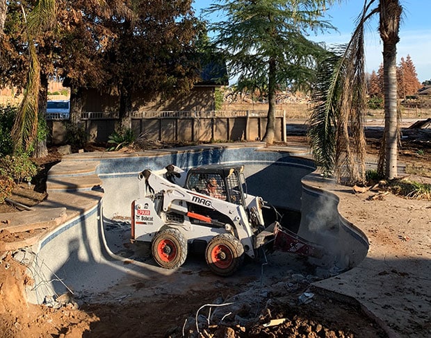 An excavator is being used for pool removal, as it digs up a swimming pool.