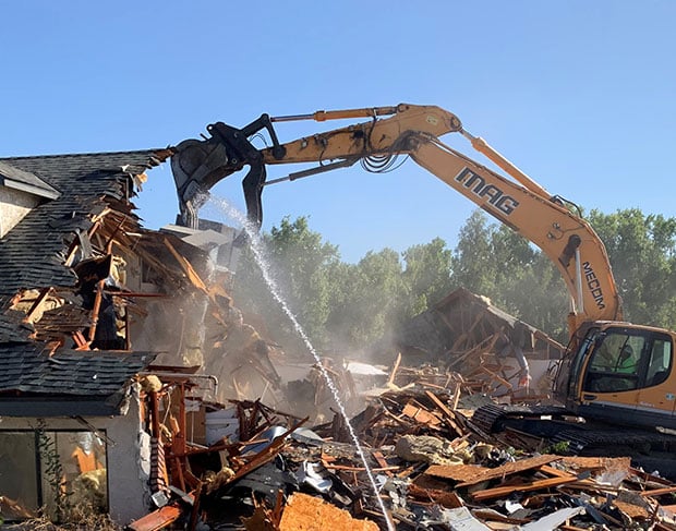 A demolition contractor is using an excavator to remove debris from a house.