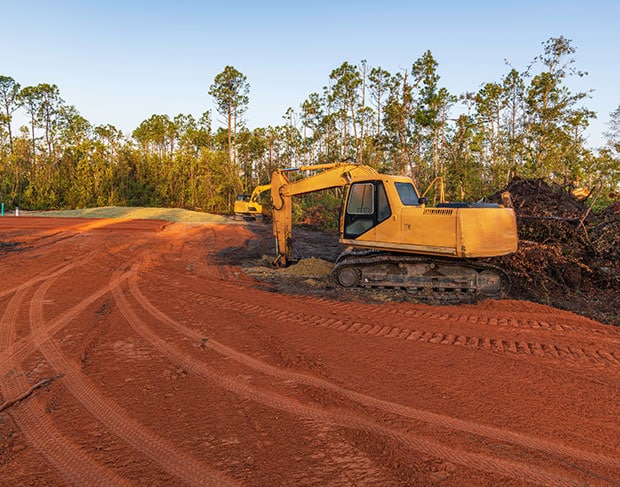 A land clearing service is using an excavator to clear a dirt road.