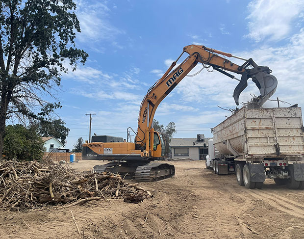 An excavator is digging up a pile of wood in need of tree removal services.