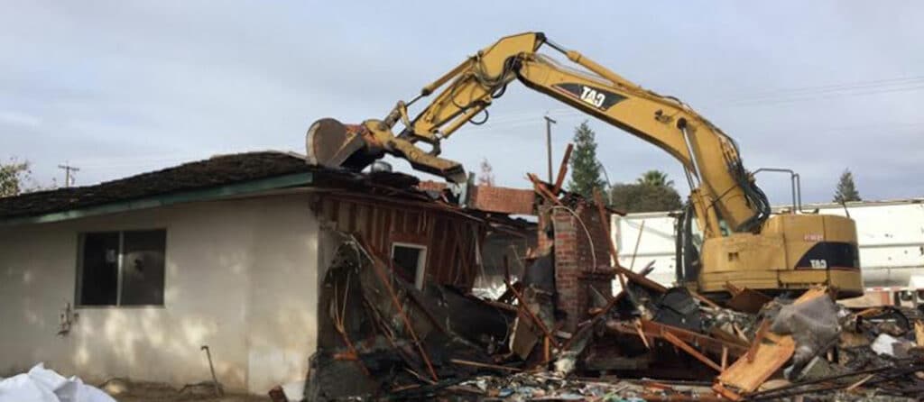 A residential demolition contractor is using an excavator to remove debris from a house.
