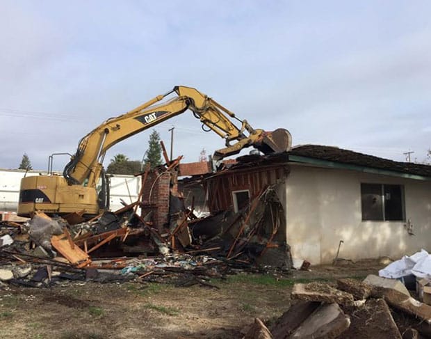 A residential demolition contractor is using an excavator to remove debris from a house.