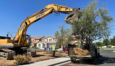 A mag engineering excavator is digging up a tree in front of a house.