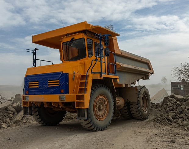 A yellow dump truck is parked on a dirt road, providing hauling services for construction projects.