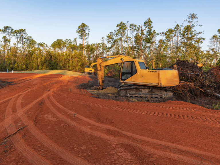 An excavator performing land clearing services on a dirt road.